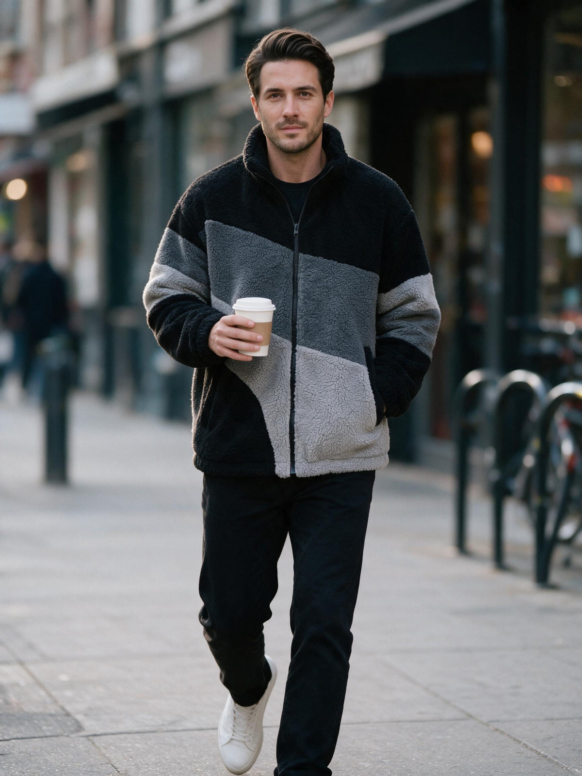 Man walking a city street with a coffee in the black and grey sherpa fleece jacket