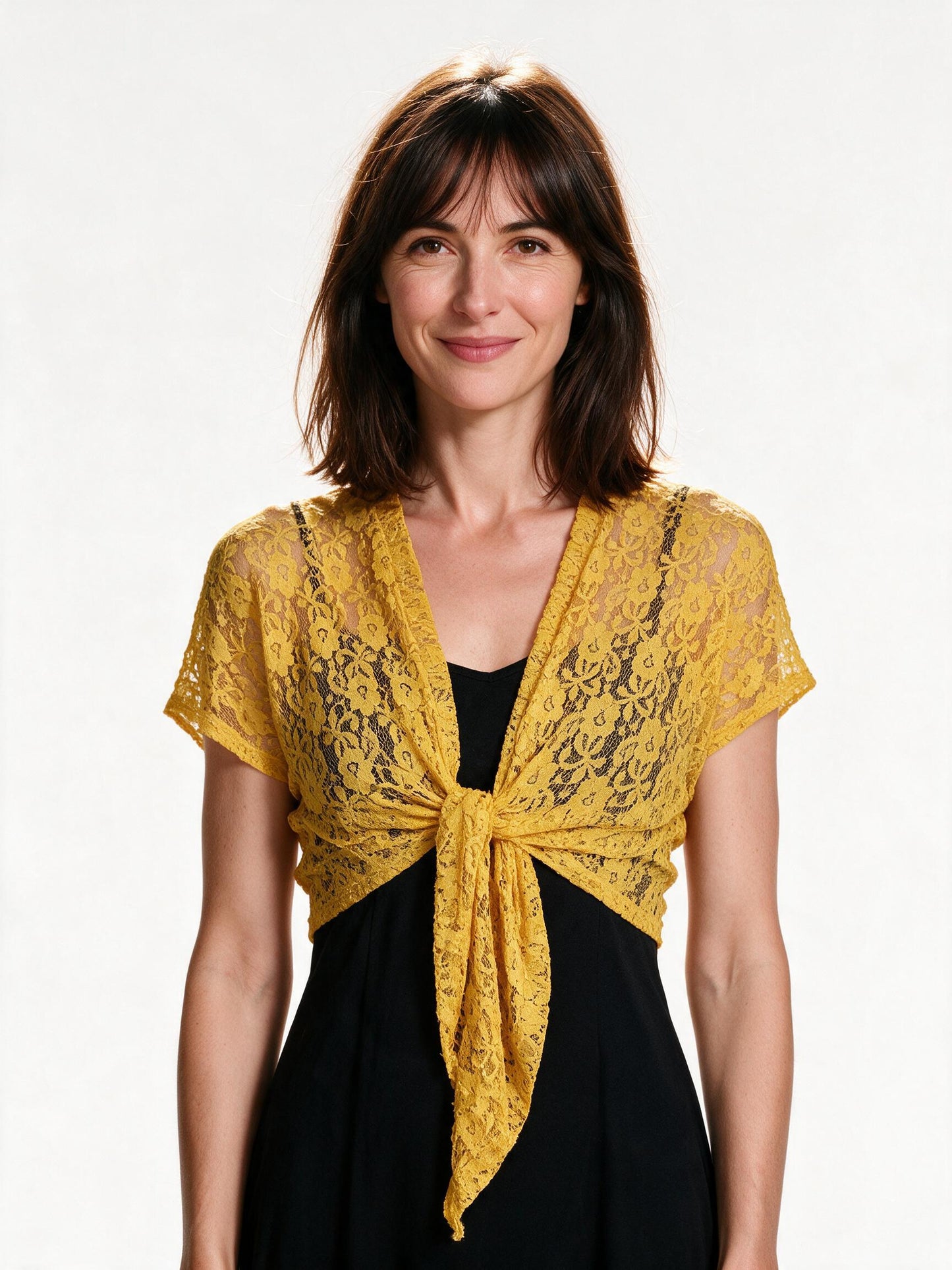 Yellow lace tie-front bolero shrug worn open over a black slip dress, white background