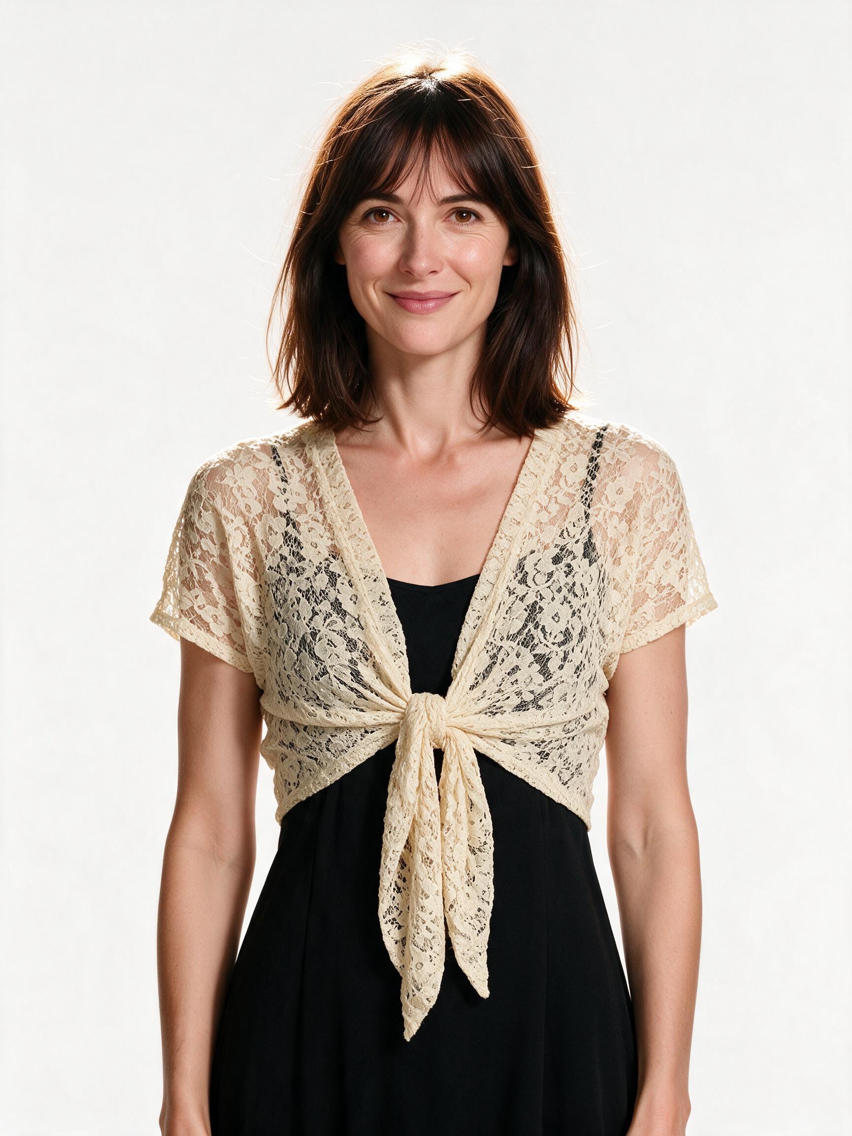 Beige lace tie-front bolero shrug worn open over a black slip dress, front view on white