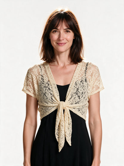 Beige lace tie-front bolero shrug worn open over a black slip dress, front view on white