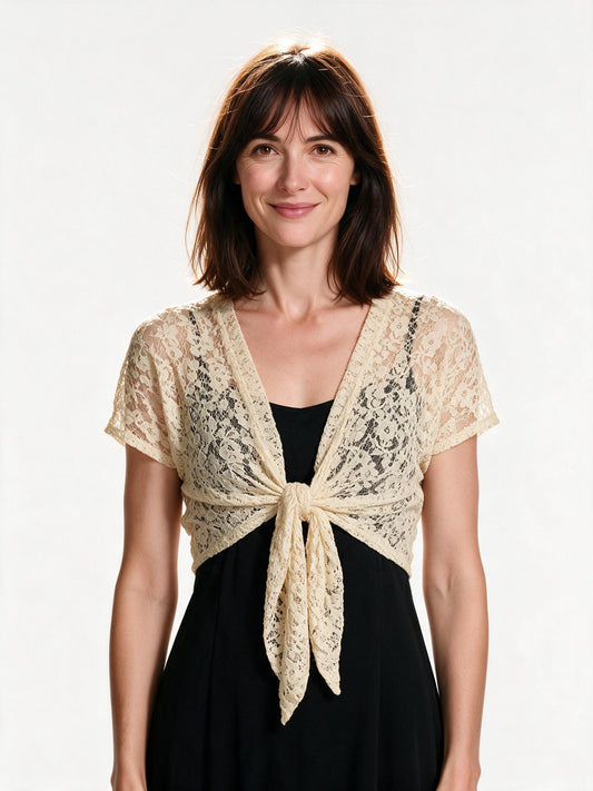 Beige lace tie-front bolero shrug worn open over a black slip dress, front view on white